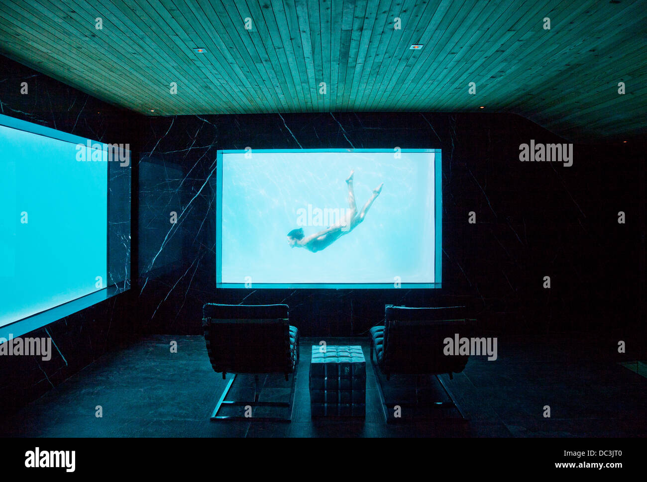 View of woman swimming underwater from window in pool room Stock Photo