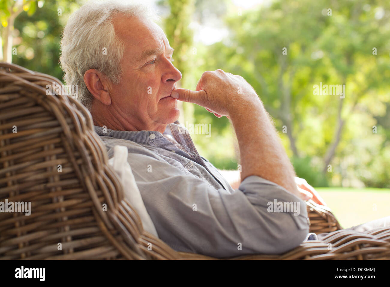 Pensive senior man sitting in wicker armchair on porch Stock Photo