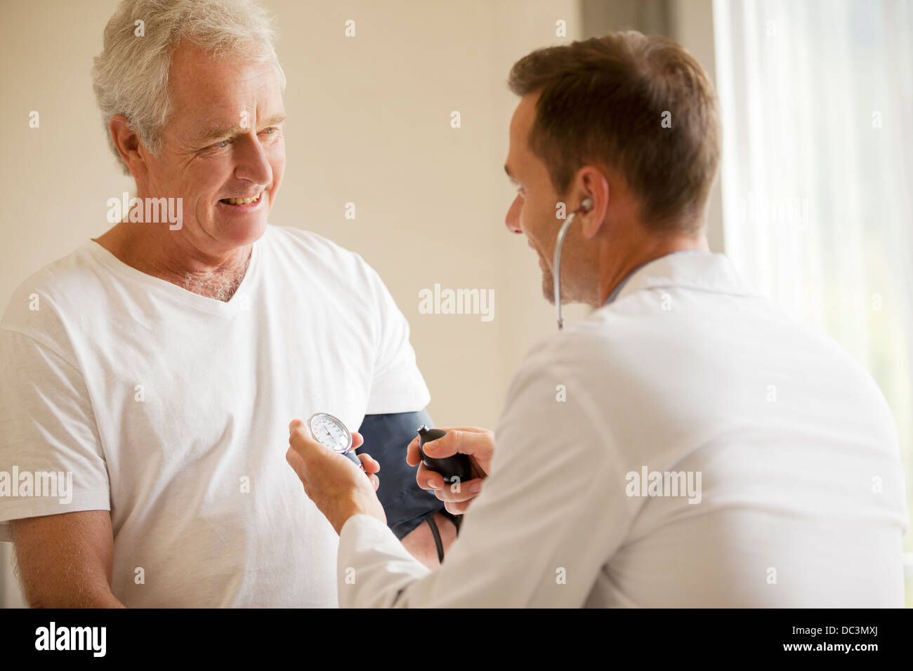 Doctor checking senior man's blood pressure in doctor's office Stock Photo