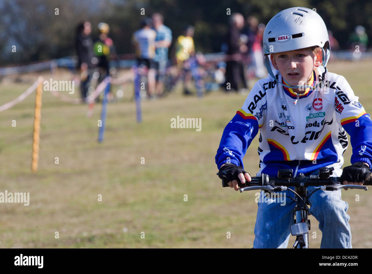 Young boy in a crash hat and cycling jersey competes in a cyclocross Stock Photo
