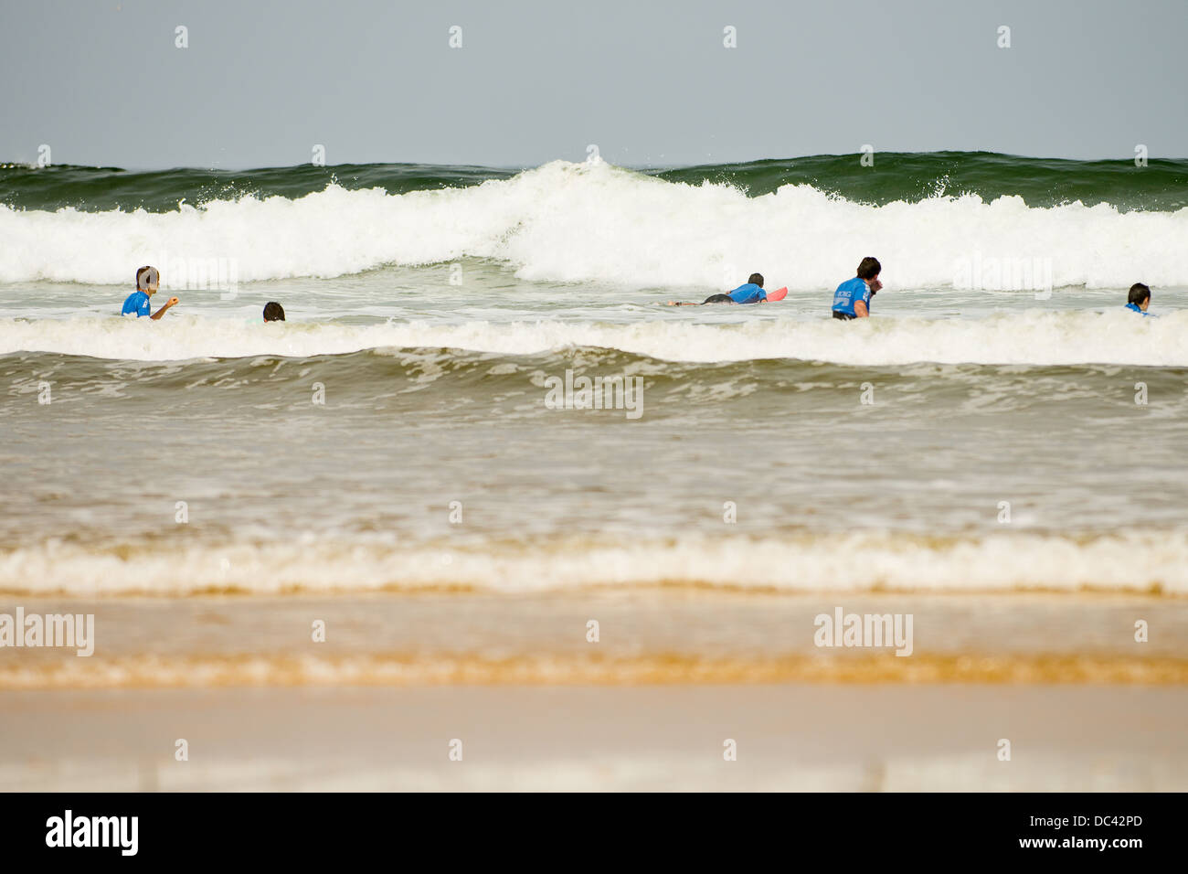People learning to surf in big waves near beach in the sun Stock Photo
