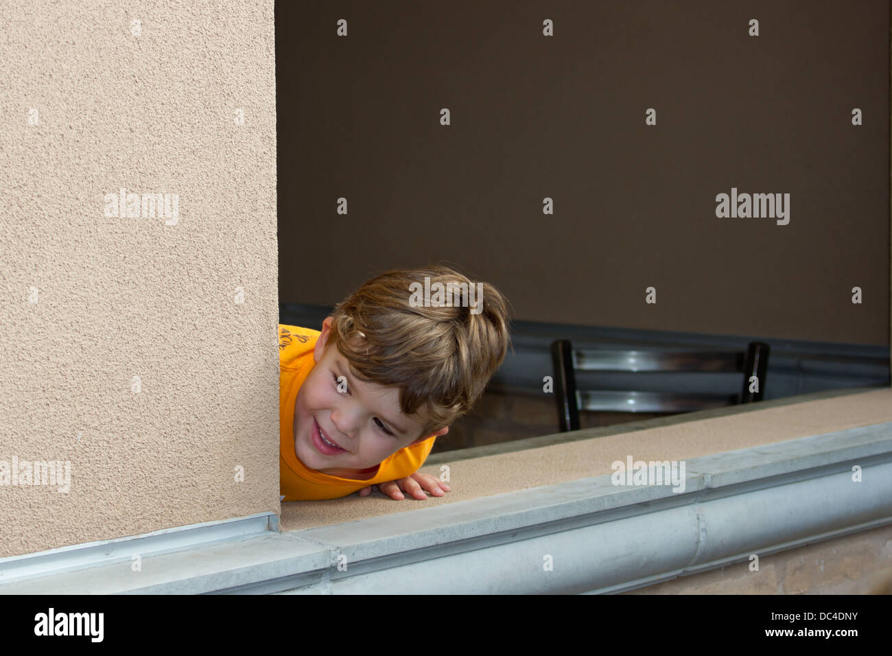 A young boy with a cute smile leaning out a window. Stock Photo