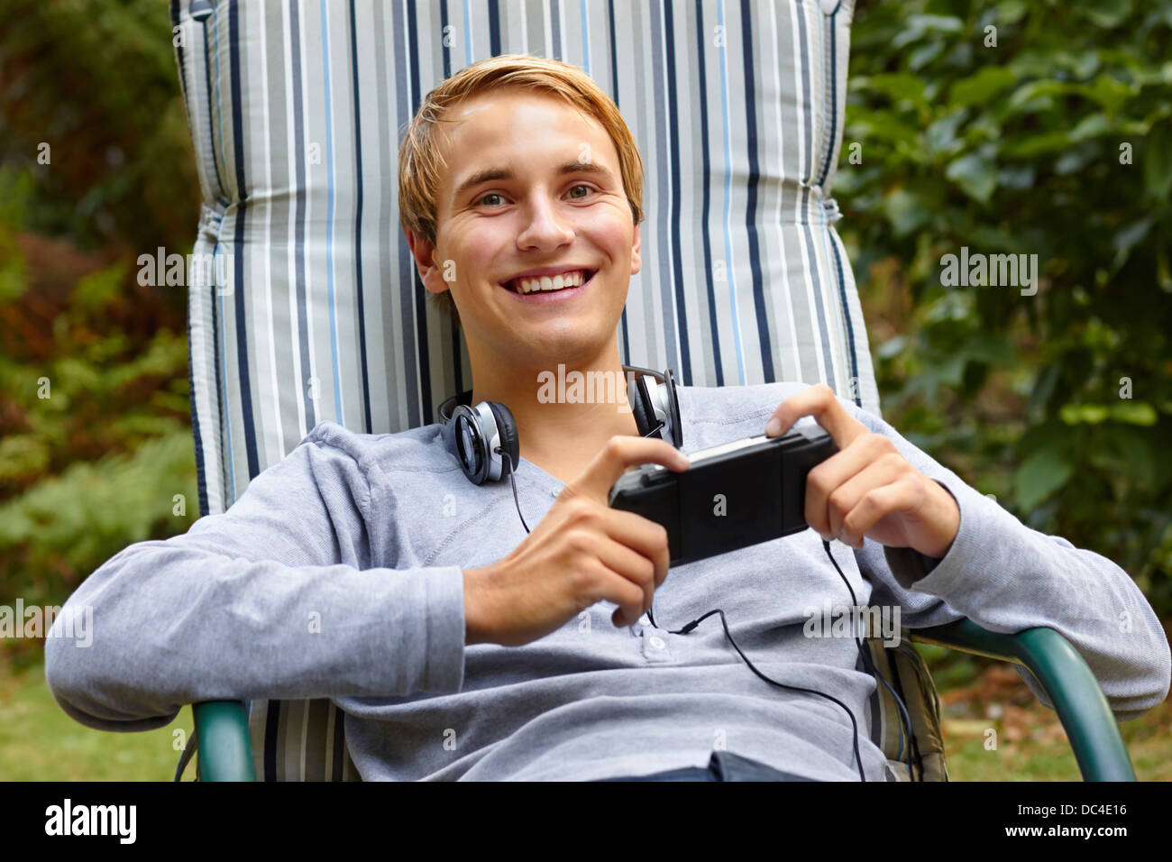 Young male relaxing in lounge outdoors with a game console and headphones. Stock Photo