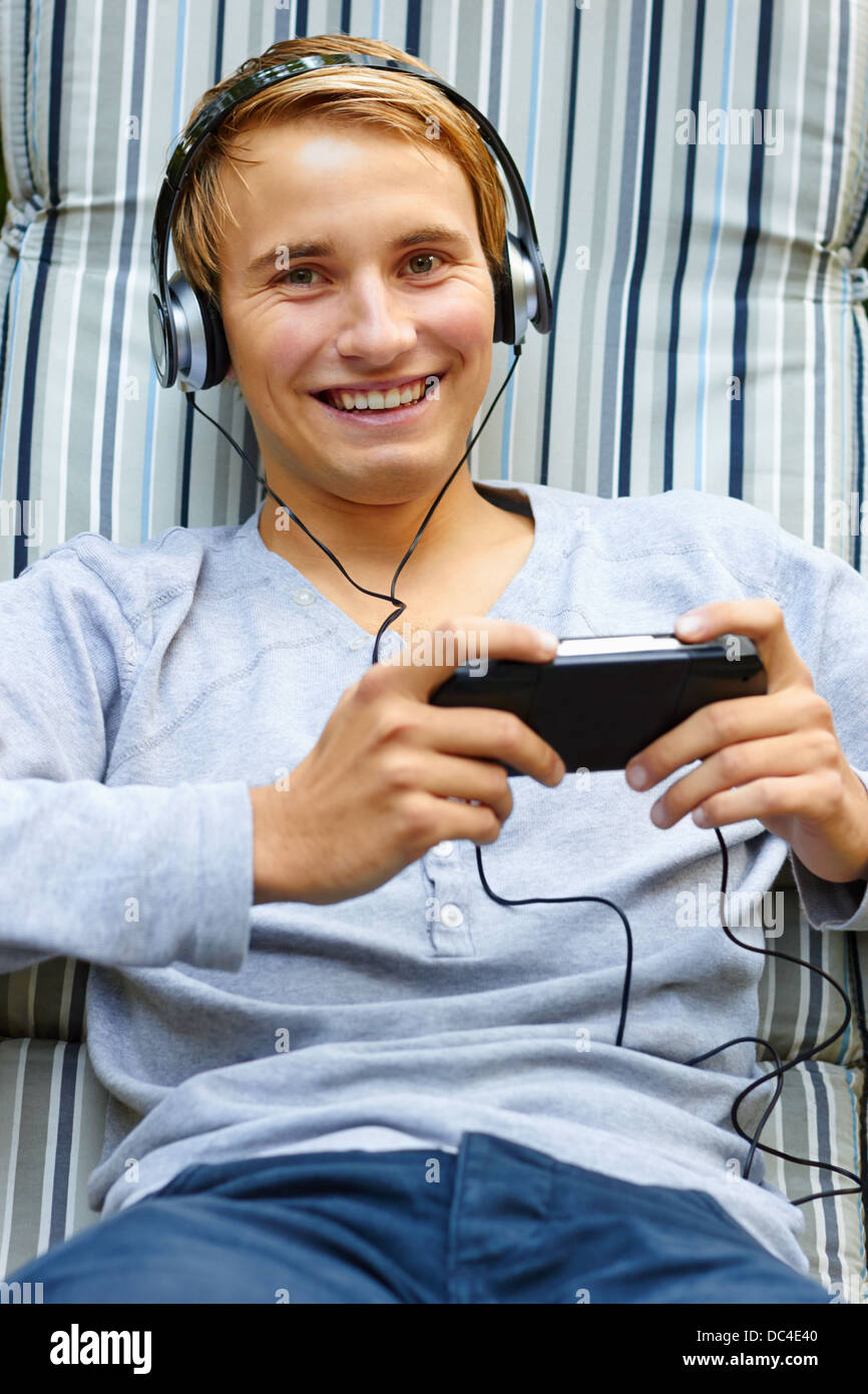 Young male chilling out to music and playing hand-held game Stock Photo