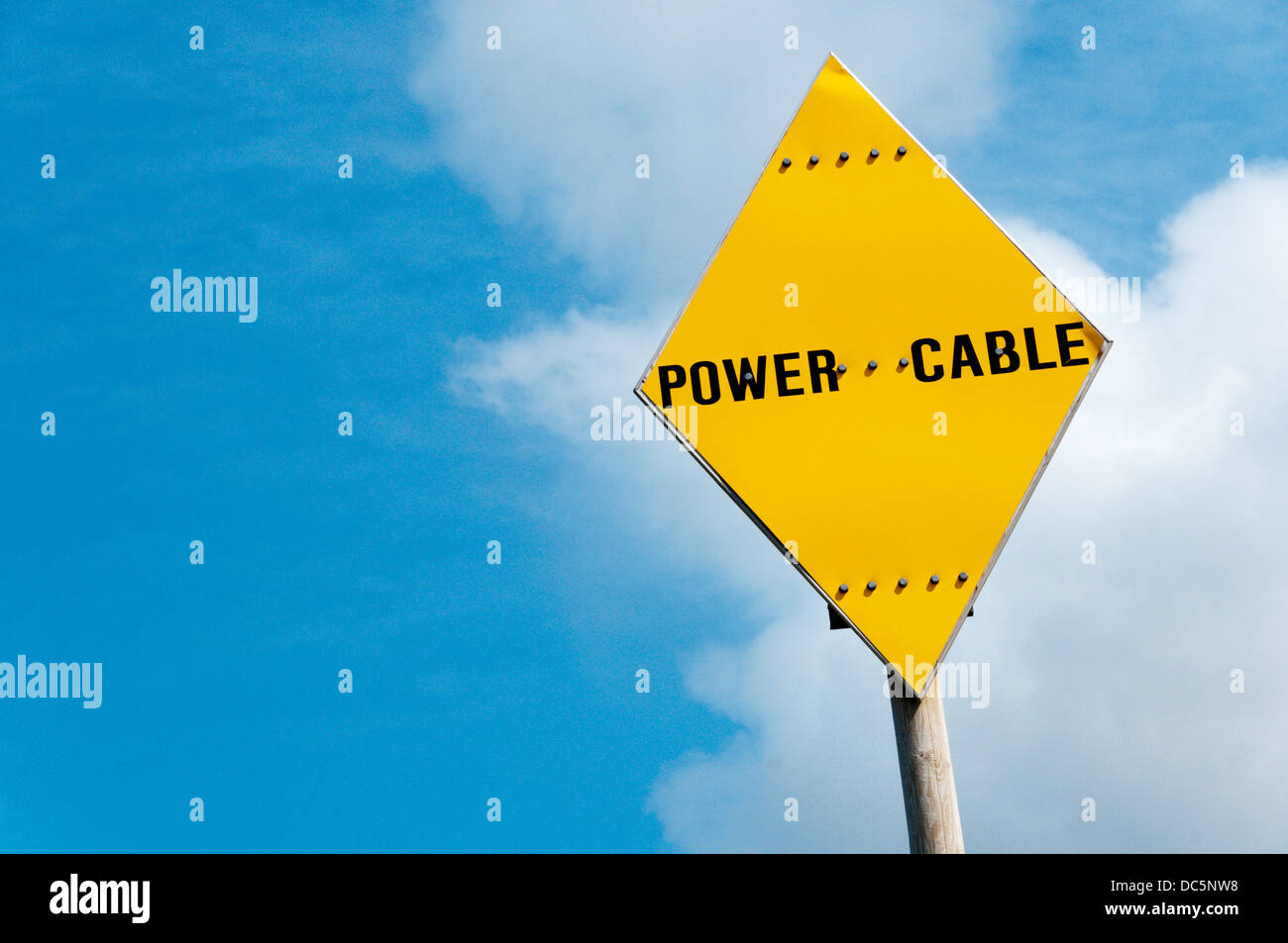 A yellow diamond-shaped Power Cable warning sign against a blue sky. Stock Photo