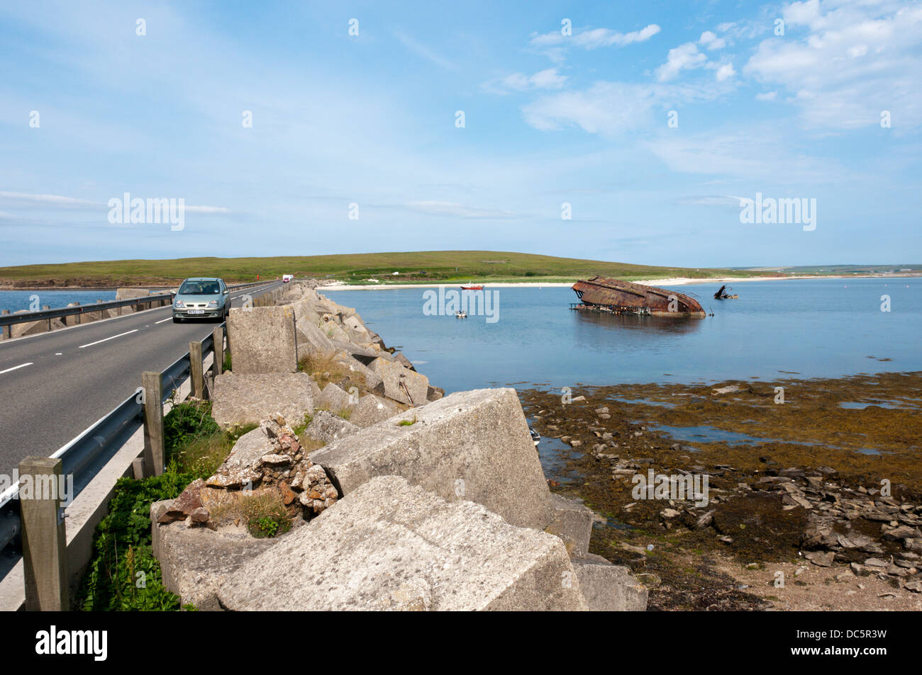 A car crossing Churchill Barrier 3 with the remains of a blockship between Glimps Holm and Burray, Orkney. Stock Photo