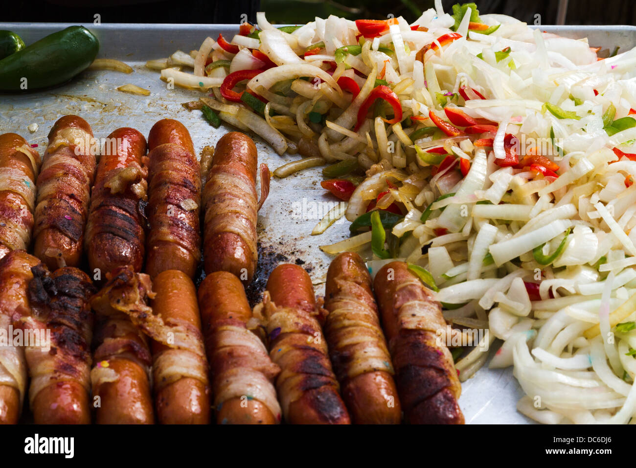 Bacon wrapped hot dogs and vegetables cooking on an outdoor grill Stock