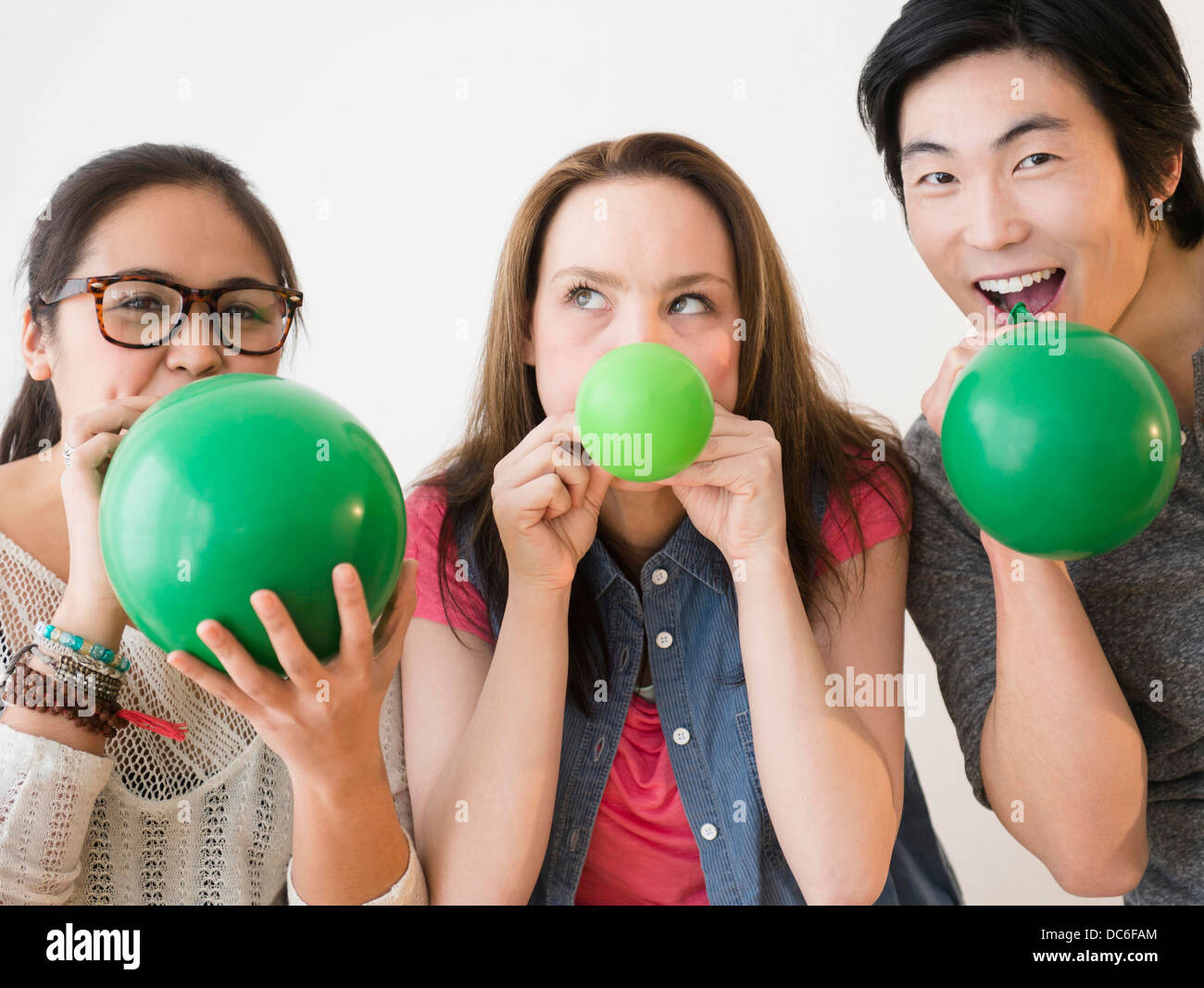 Portrait of young women and man blowing green balloons Stock Photo
