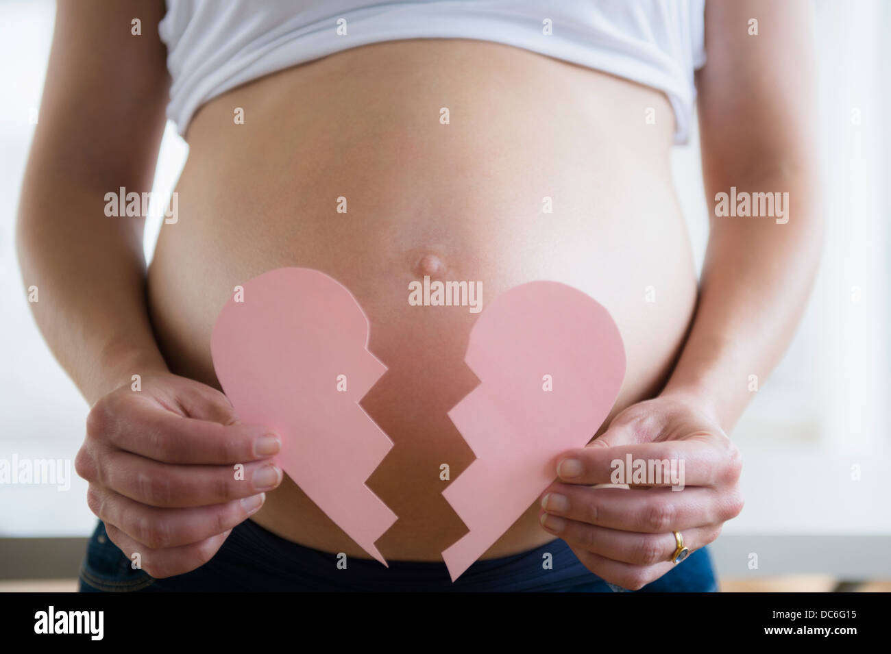 Mid section of pregnant woman holding broken paper heart Stock Photo