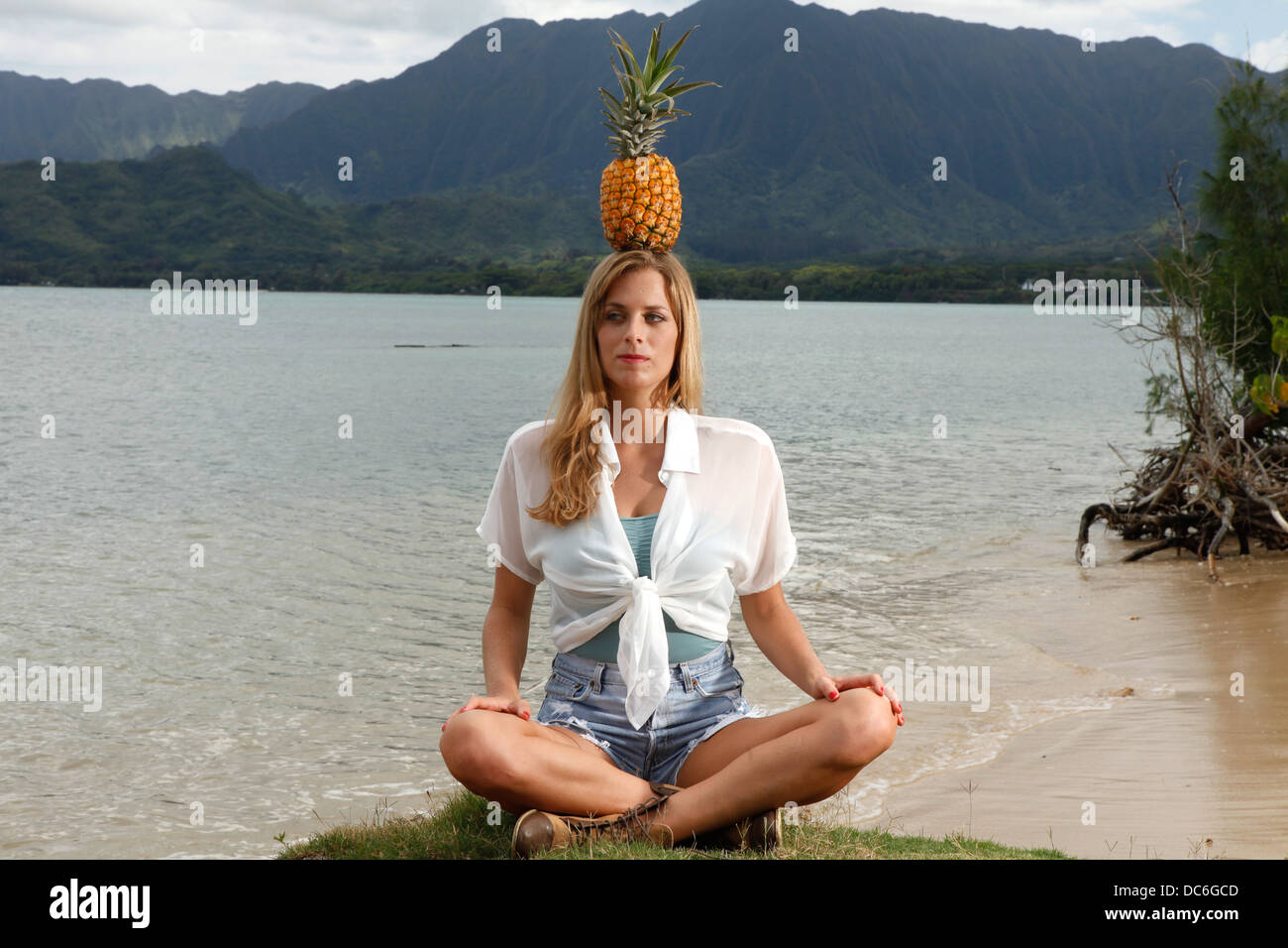 A young caucasian woman meditates with a pineapple balancing on top of her head in Honolulu, Hawaii. Stock Photo