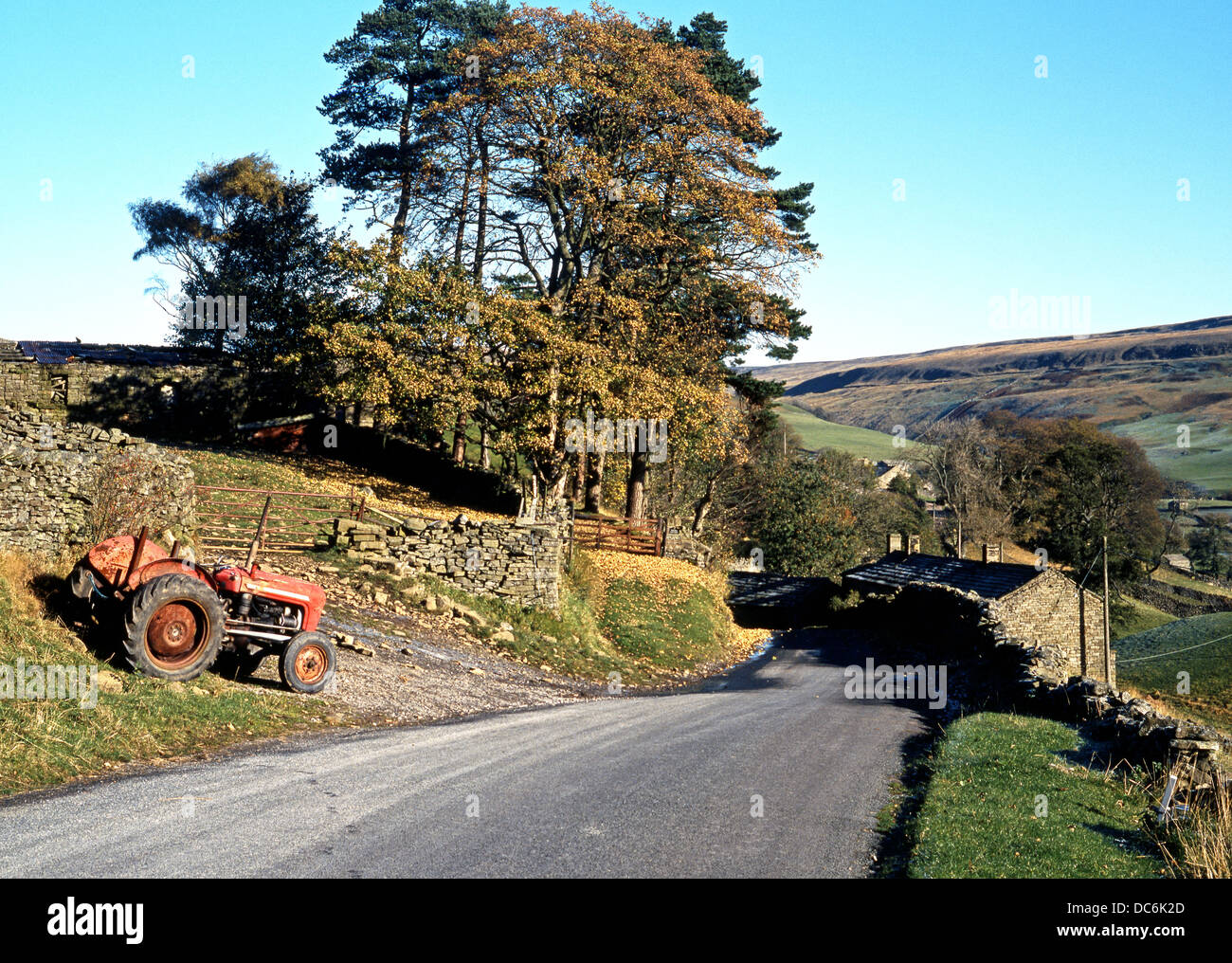 Tractor parked by a dry stone wall with a vie towards the village and farmhouses, Thwaite, Yorkshire Dales, North Yorkshire, UK. Stock Photo