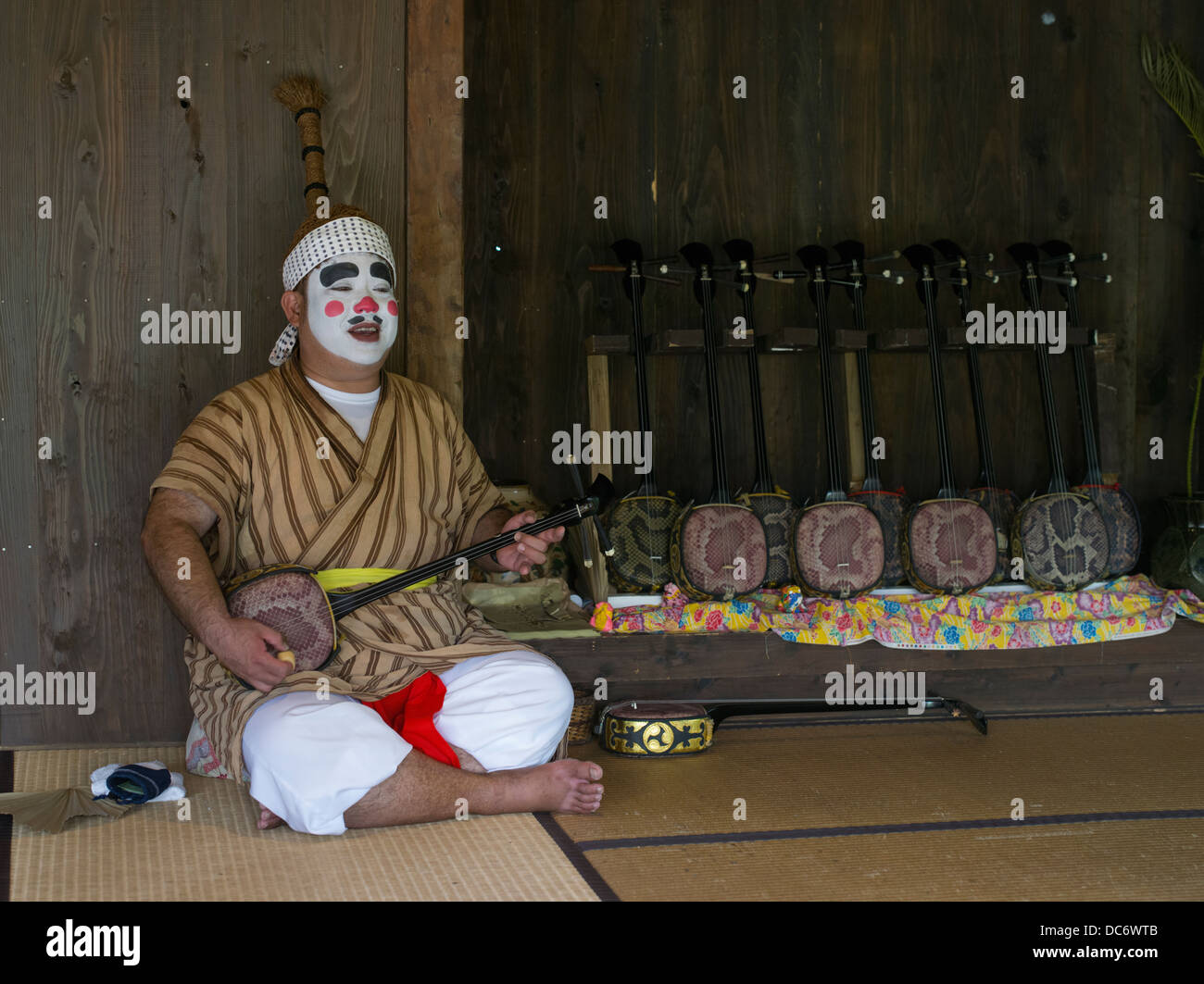 Okinawan man dressed as Chondara clown with sanshin at Ryukyu Mura a ...