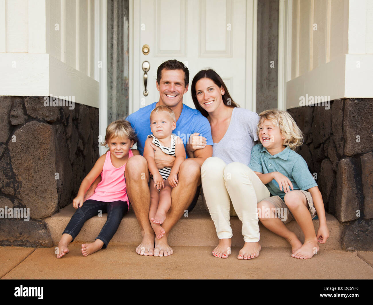 Family with three kids (6-7, 2-3, 6-11 months) sitting in front of house Stock Photo