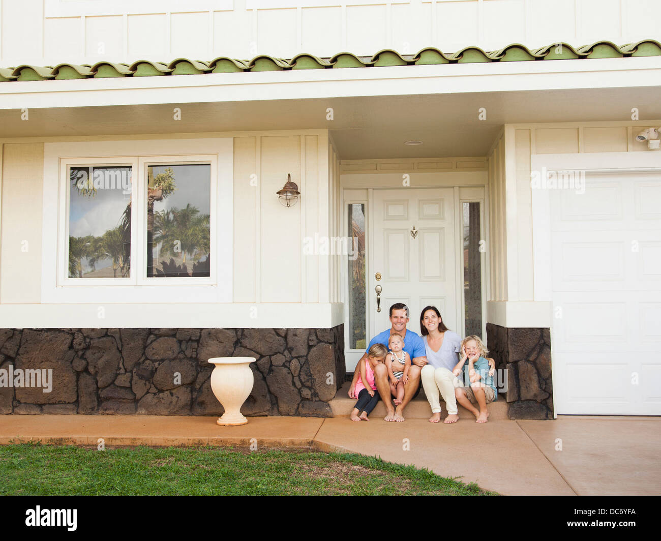 USA, Hawaii, Kauai, Family with three kids (6-7, 2-3, 6-11 months) sitting in front of house Stock Photo