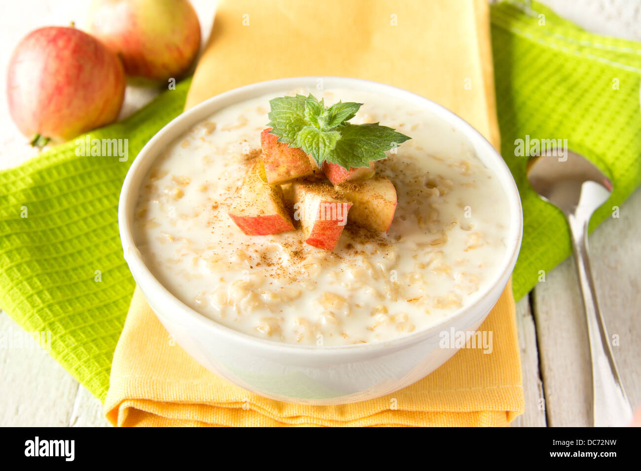 Fresh tasty hot oatmeal porridge with apple slices, mint, cinnamon and spoon on napkin and wooden table. Healthy natural vegetar Stock Photo
