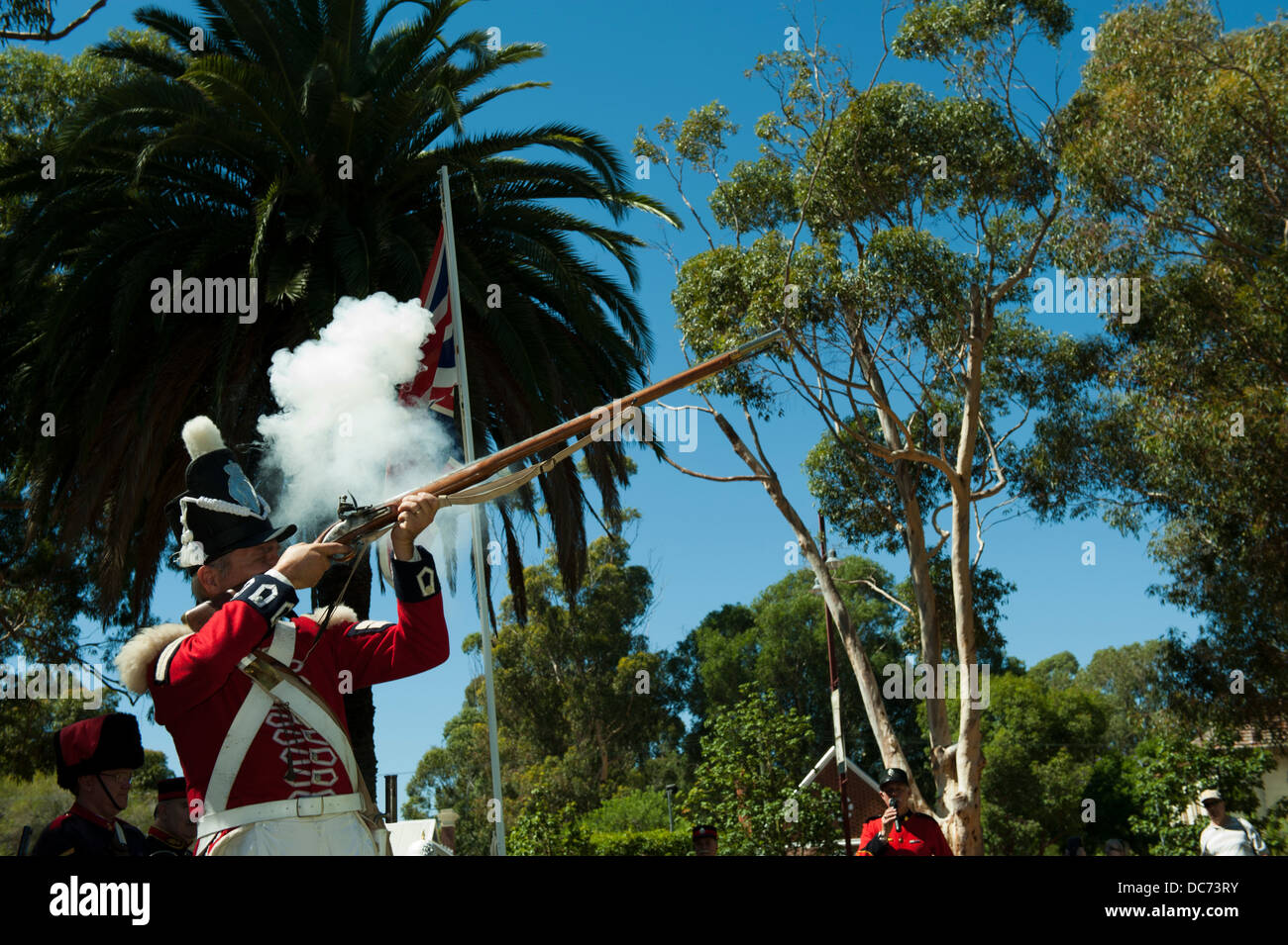 Adult man in period military costume, firing a muzzle-loading musket, face covered in smoke from cartridge ignition. Stock Photo