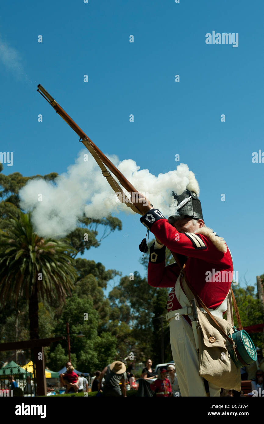 Adult man in period military costume, firing a muzzle-loading musket, face covered in smoke from cartridge ignition. Stock Photo