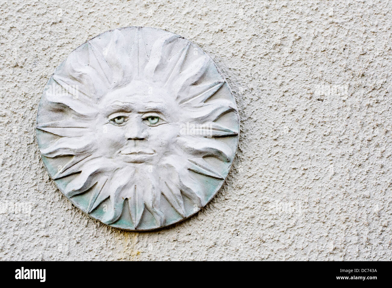 Stylised sun face plaque on a white textured wall. Stock Photo