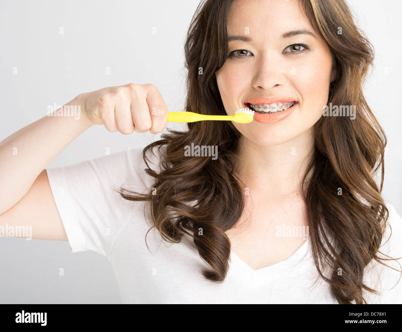 Beautiful Asian American girl with white t-shirt and orthodontic braces brushing teeth Stock Photo