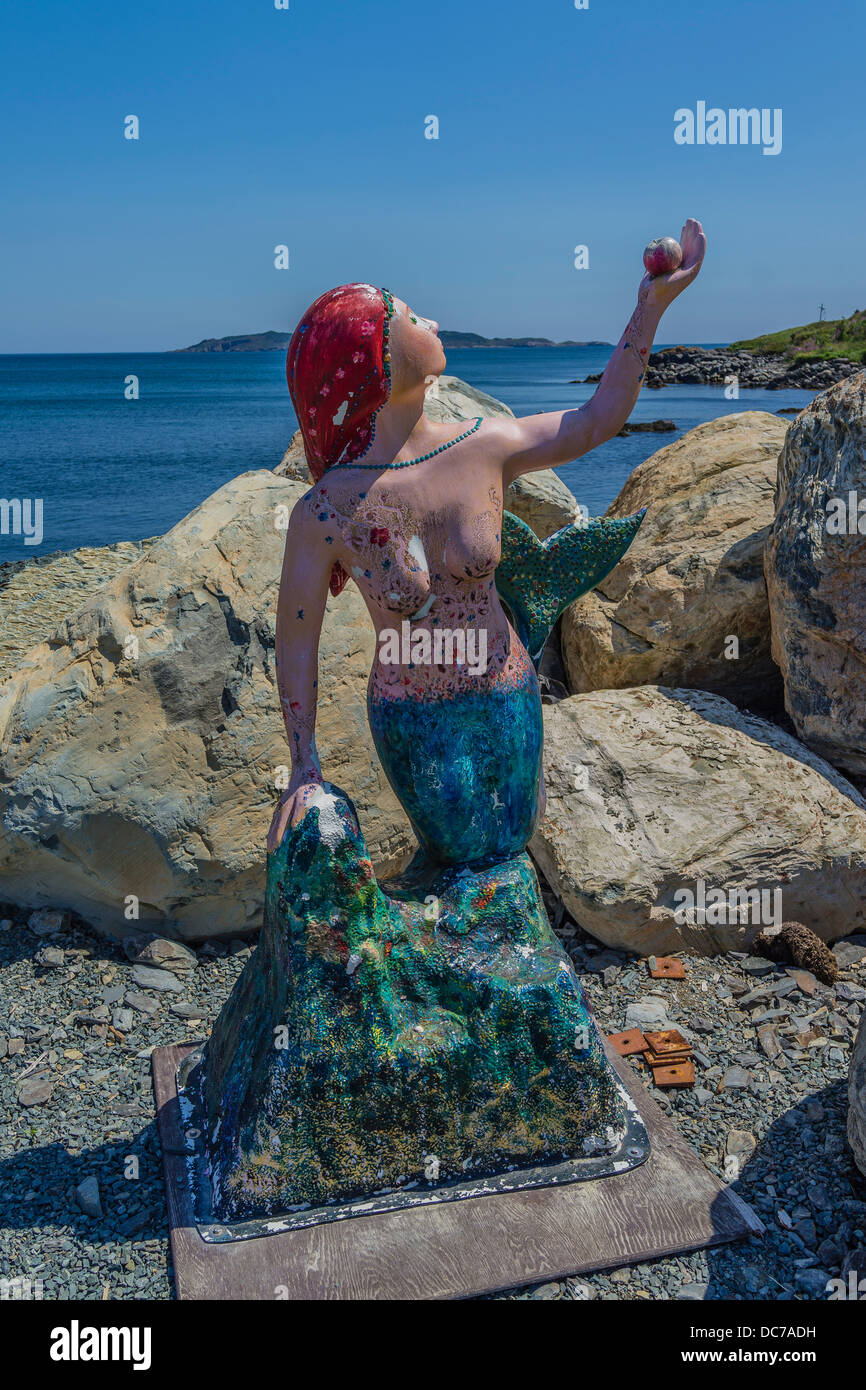 A mermaid sculpture, with the mermaid gesturing with arm extended upward at the harbor at