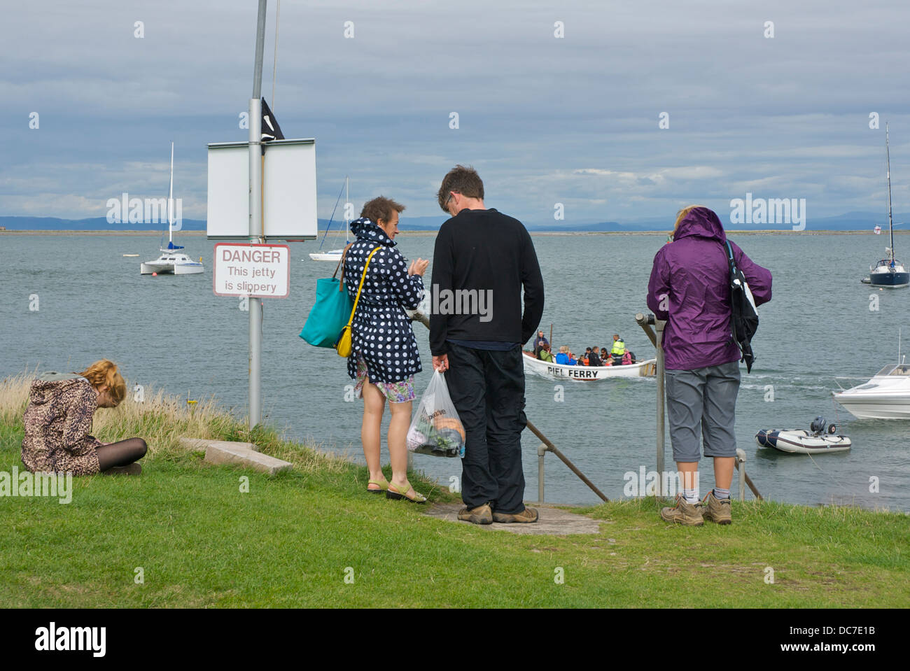 Four people waiting for the ferry to return, Piel Island, South Lakeland, Cumbria, England UK Stock Photo