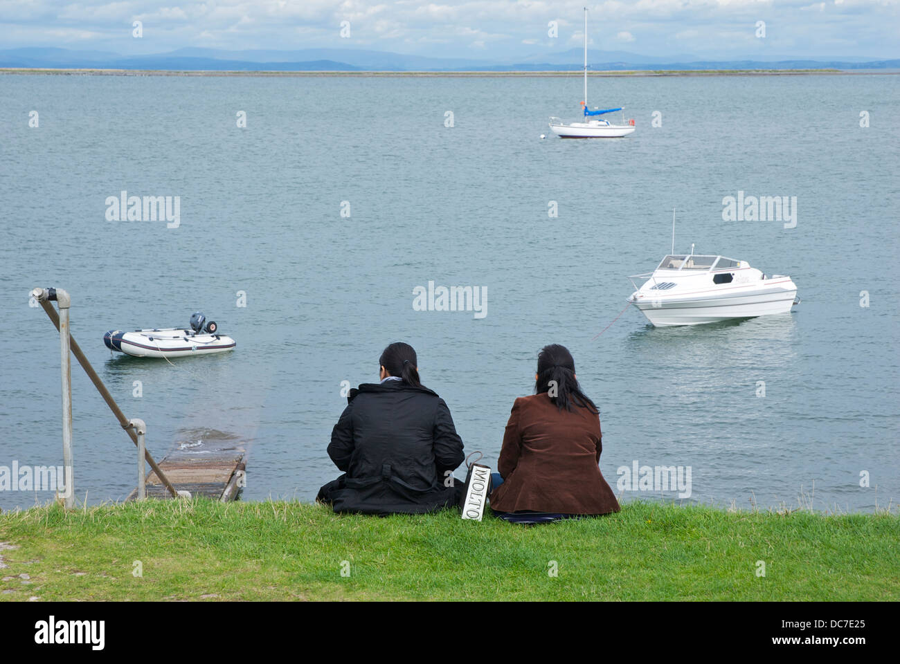 Two women sitting on grassy bank, Piel Island, South Lakeland, Cumbria, England UK Stock Photo