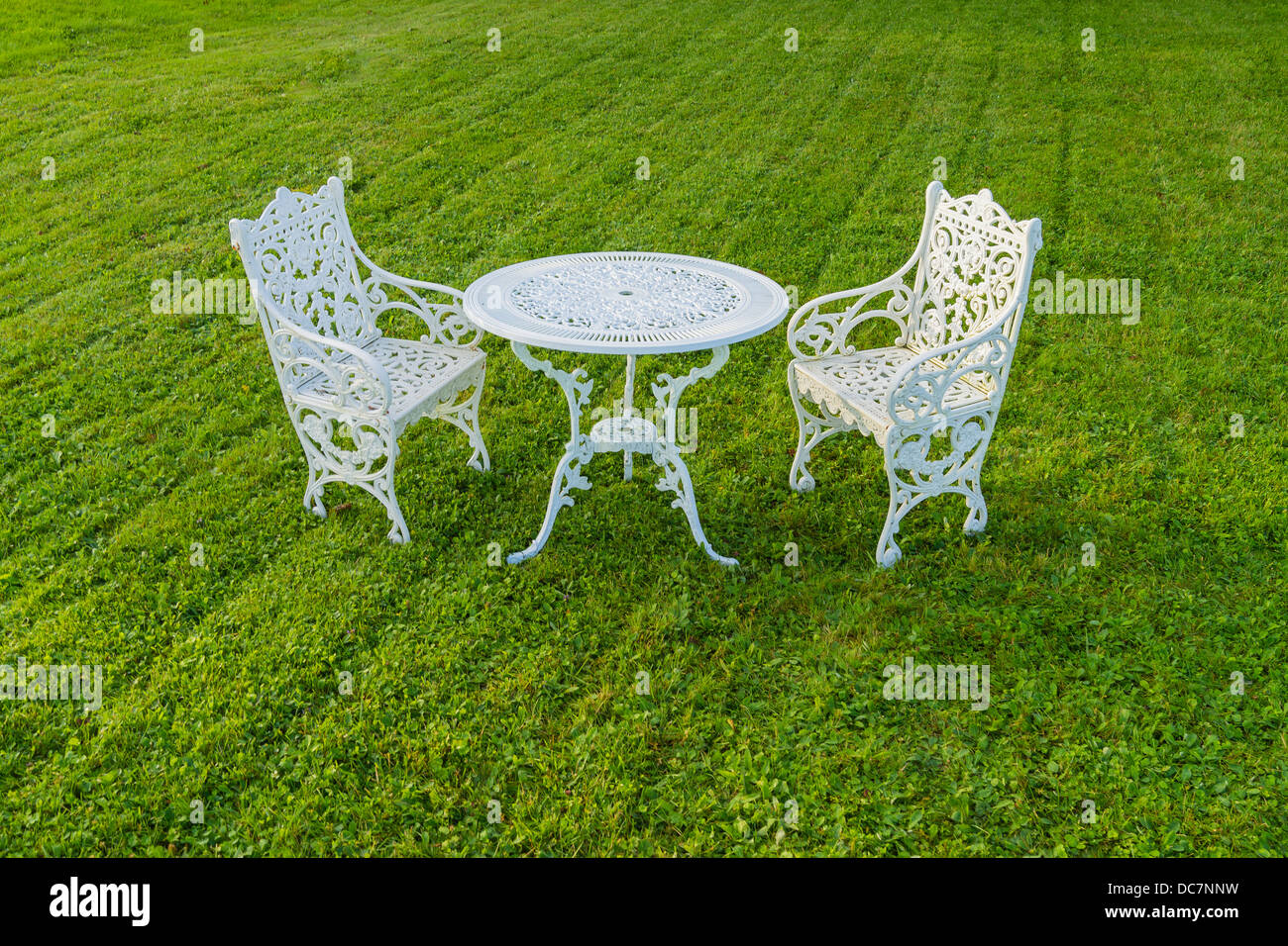 Two white iron lawn chairs & white iron table on manicured green lawn