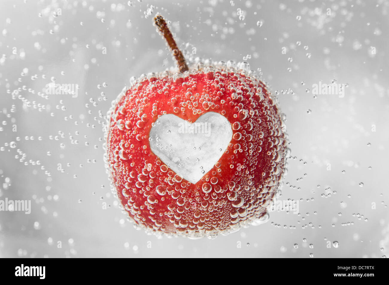 Red Apple with heart-shape cut-out in middle, floating in bubbly water. Stock Photo