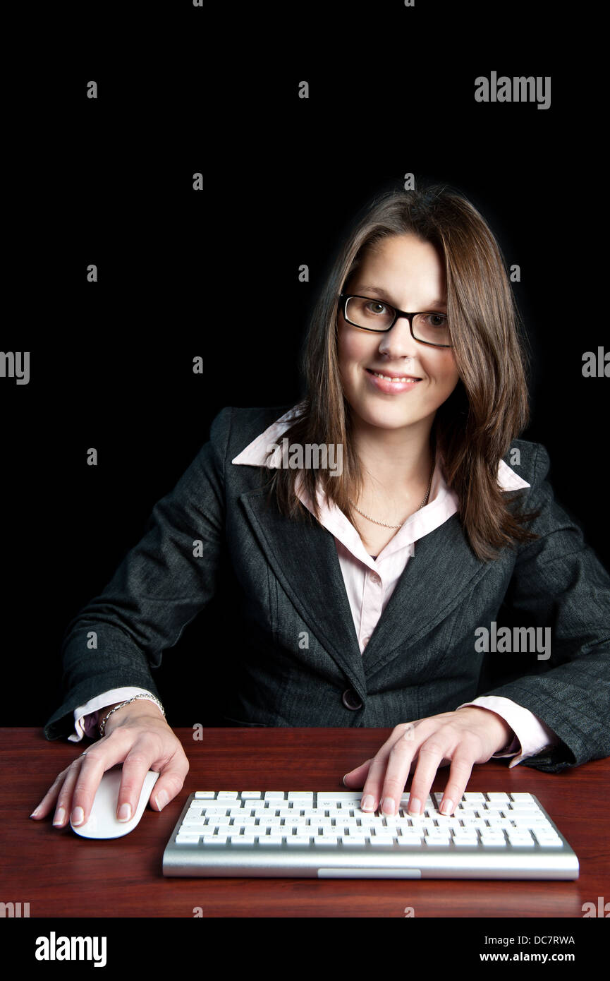 Attractive young professional corporate woman sitting behind her desk with computer keyboard and mouse. Stock Photo