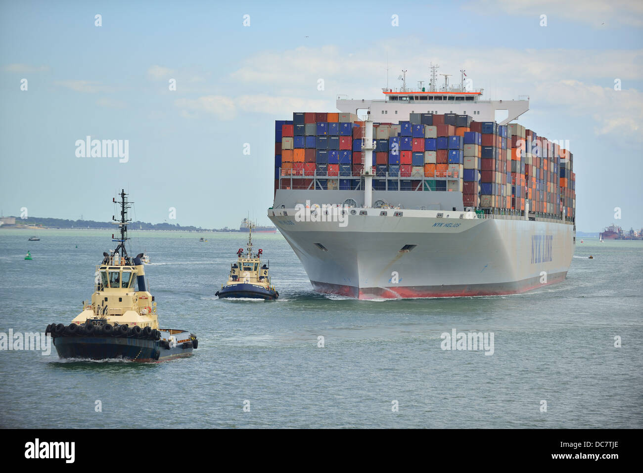 Container ship in Southampton Water, with two tugs assisting ship to its docking berth at