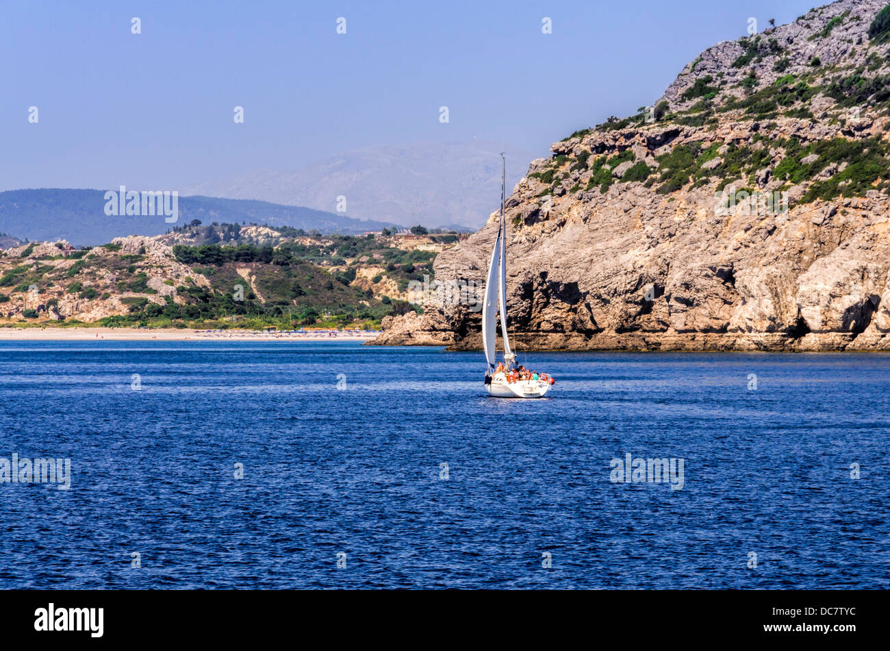 Yacht loaded with holidaymakers sailing towards a rocky island through a calm blue ocean Stock Photo