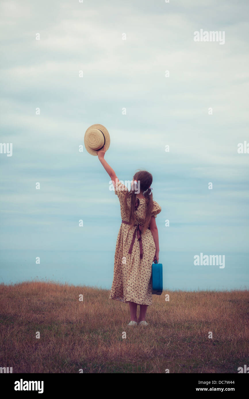 a girl in a vintage dress with suitcase holding a hat Stock Photo
