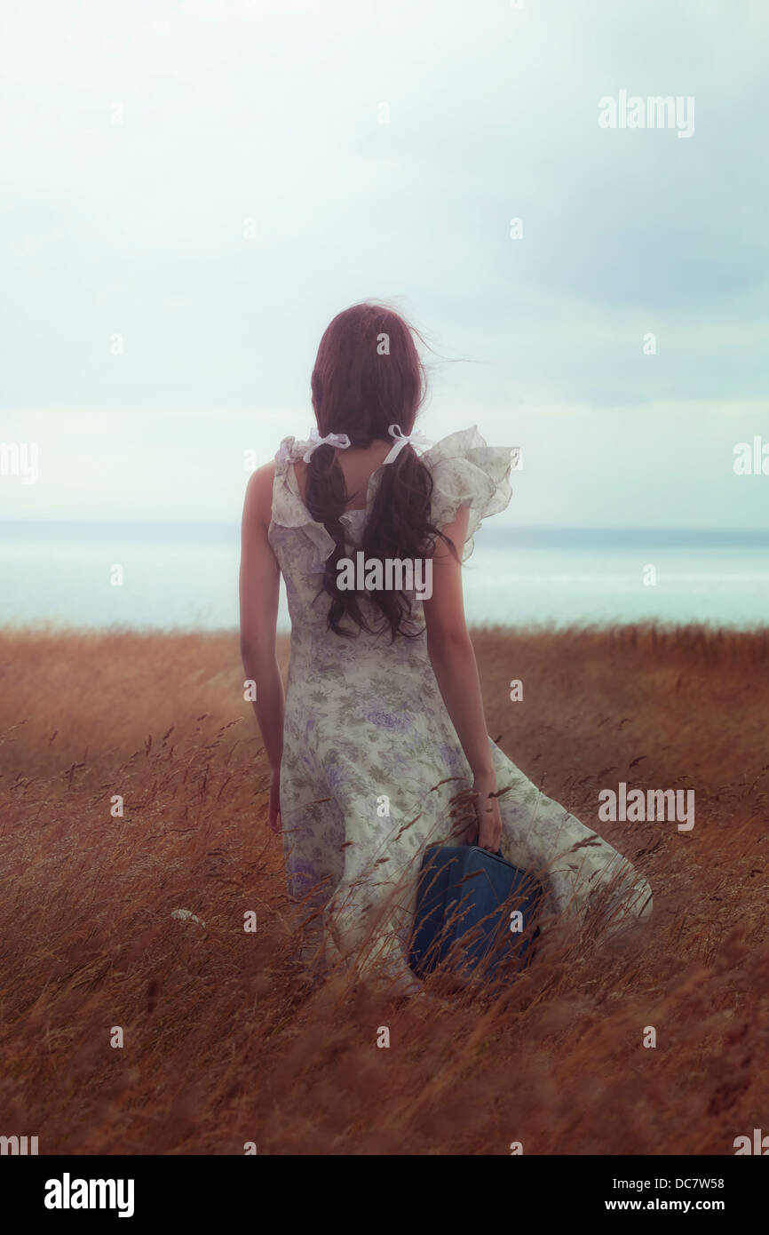 a girl in a floral dress on a field with a suitcase Stock Photo