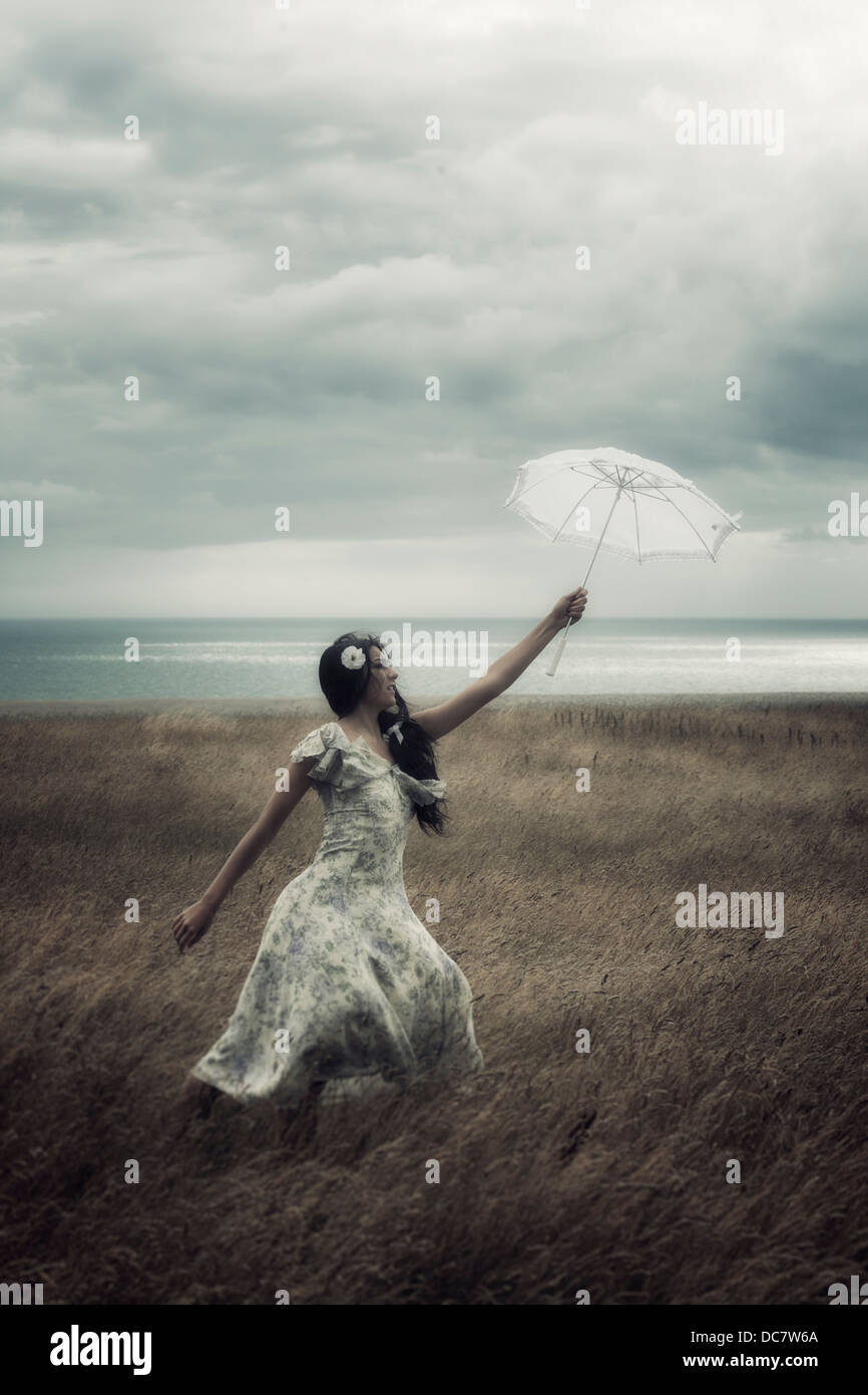 a girl in a floral dress on a field with a parasol is fighting against the wind Stock Photo