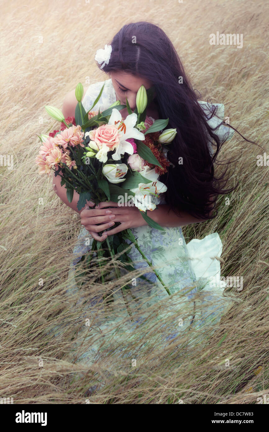 a girl sitting in a field with a bouquet of flowers Stock Photo