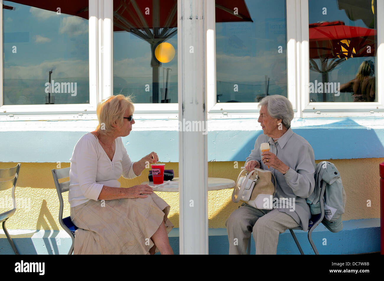 Two elderly ladies sitting in seafront café enjoying ice cream and cold drink Stock Photo