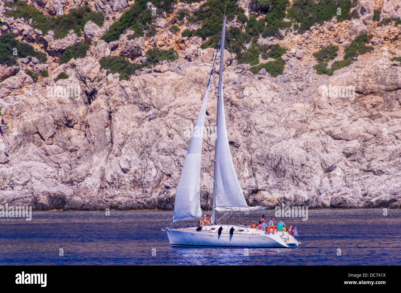 People enjoying a cruise on a pleasure yacht sailing past the base of a rocky marine cliff on a sunny summer day Stock Photo