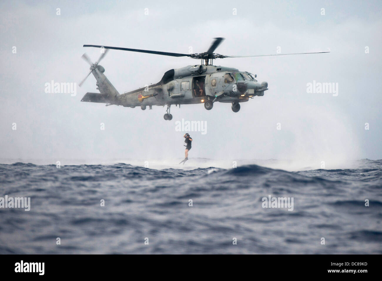 A US Navy search and rescue swimmer jumps into the ocean from an Stock