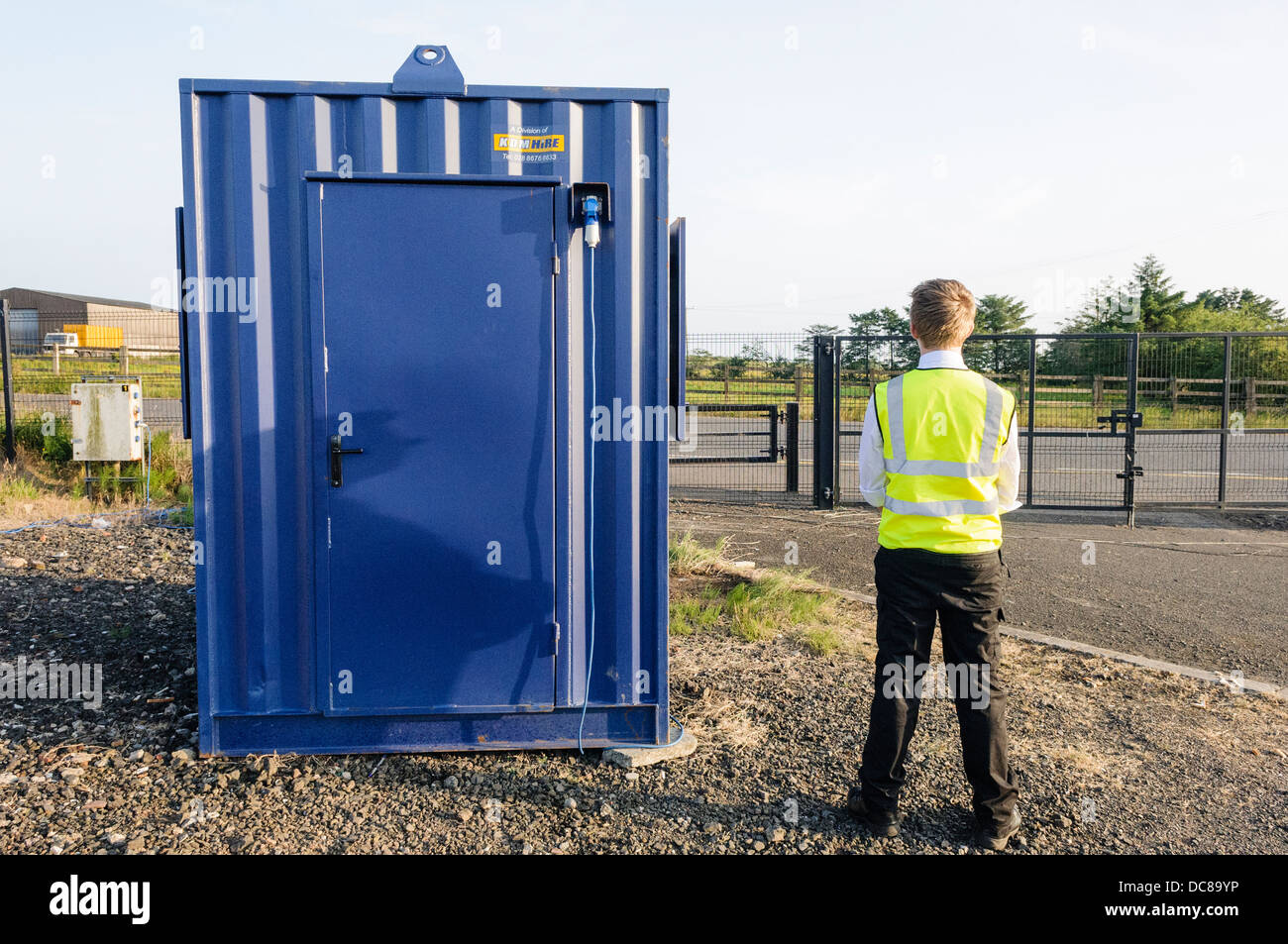 A security guard stands beside his hut inside a fenced off construction site compound Stock Photo