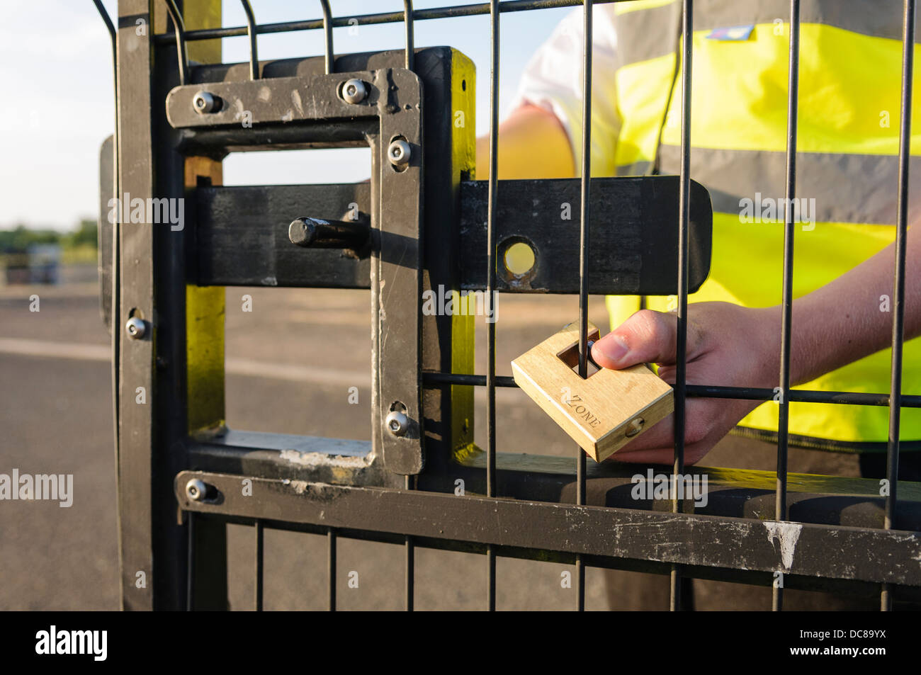 A security guard attaches a lock to a gate after unlocking the bolt and opening the gate Stock Photo