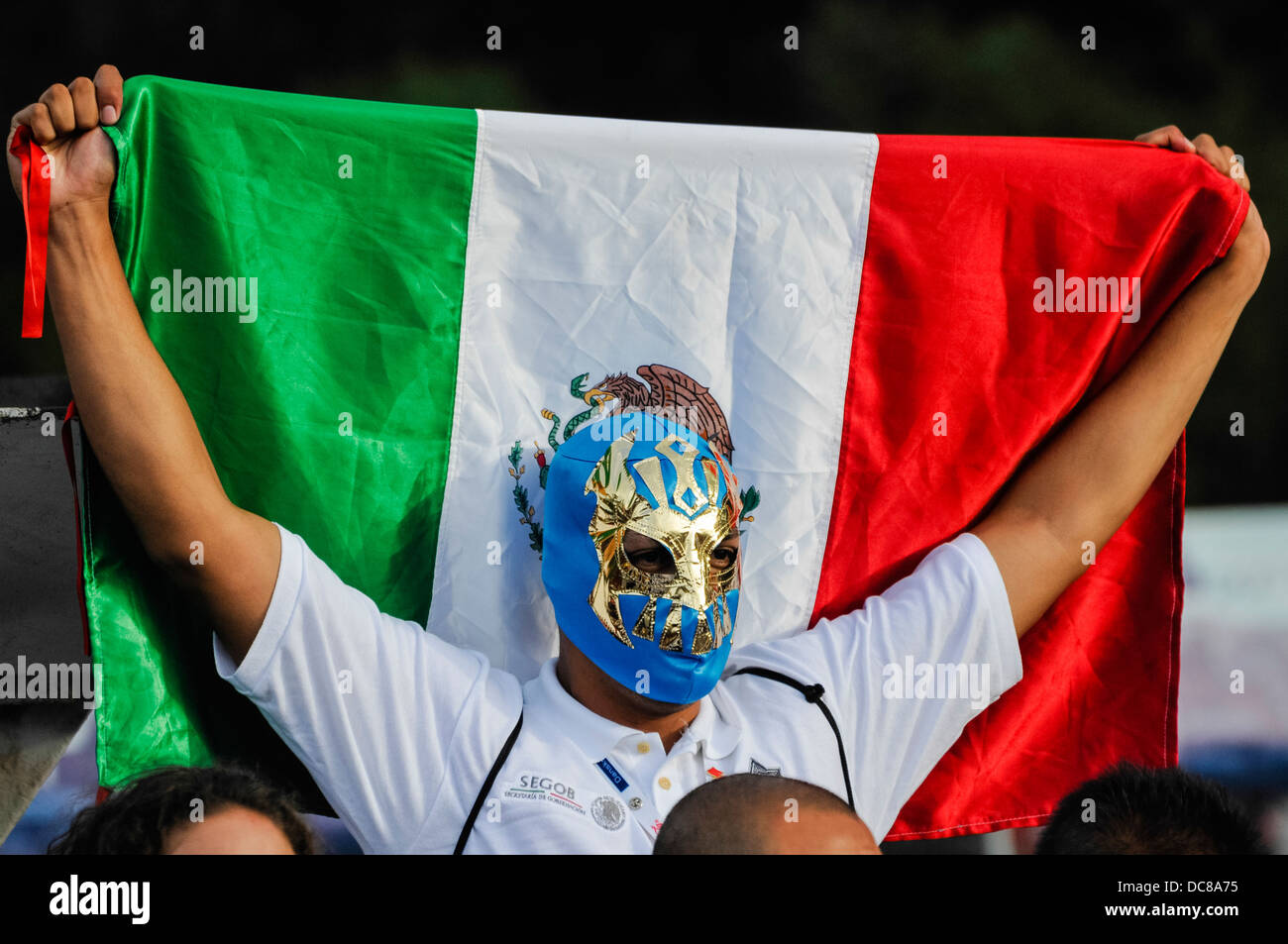 A man wears a Mexican wrestler's mask and holds up a Mexican flag Stock Photo