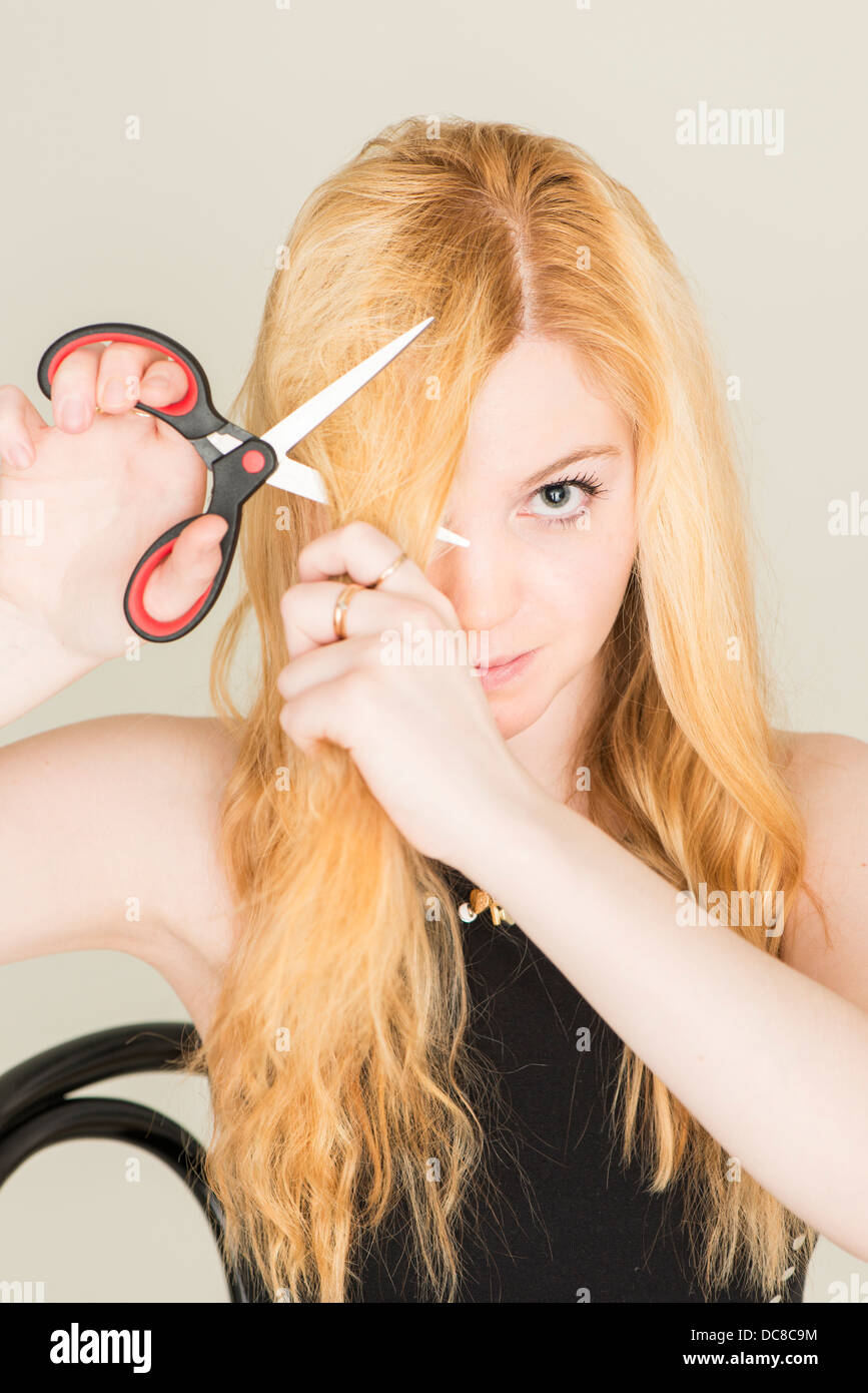 Portrait of young blond female teenager cutting her hair with scissors Stock Photo