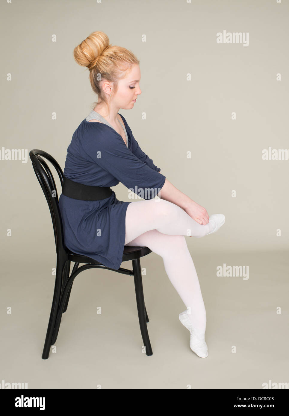 Young blond female teenager in ballet dress sitting on chair massaging foot Stock Photo
