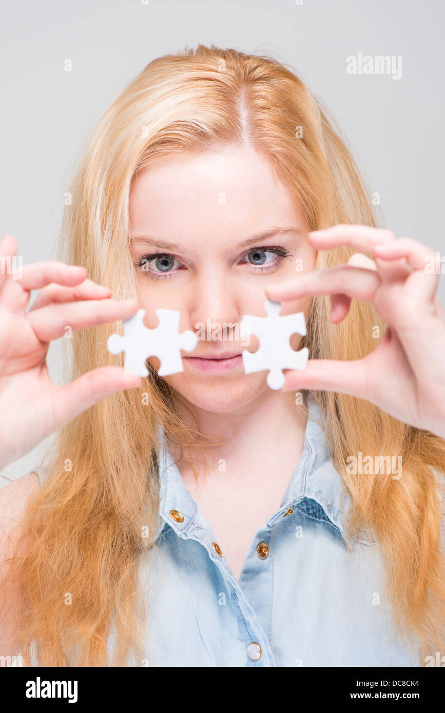 Young blonde woman holding and examining two white puzzle pieces Stock Photo