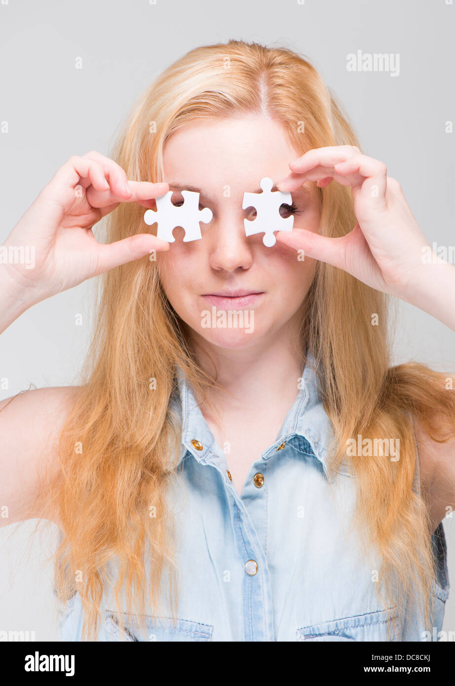 Young blonde woman holding two white puzzle pieces in front of her eyes Stock Photo