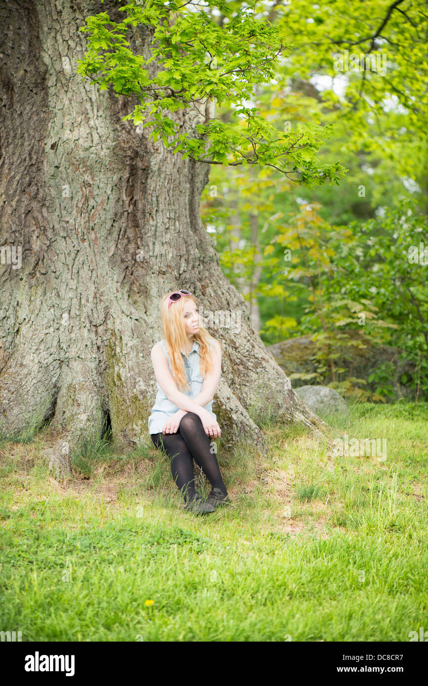 Nature scene with one young attractive woman sitting by a tree in a park Stock Photo