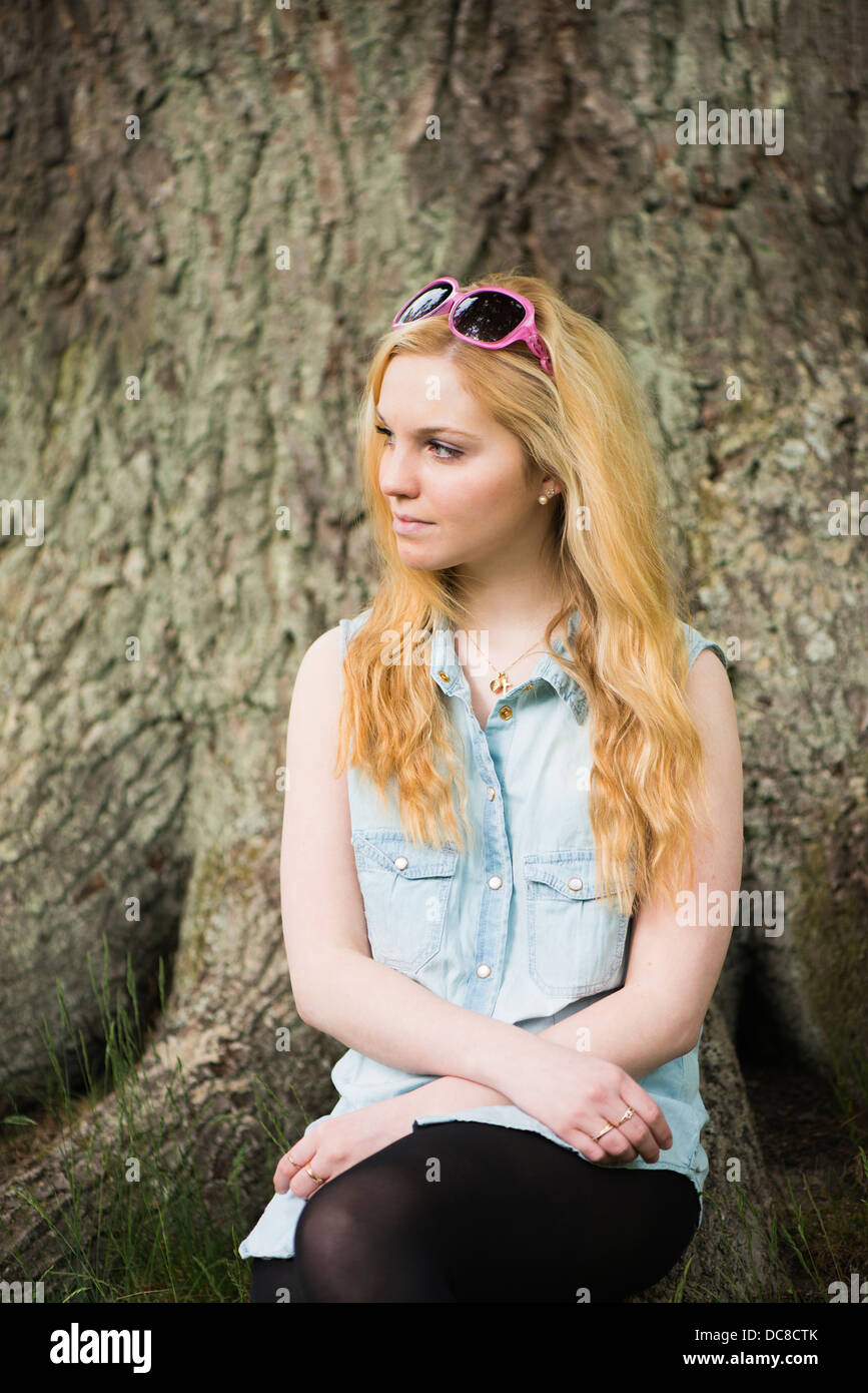 One young blonde attractive woman in front of tree in a park Stock Photo