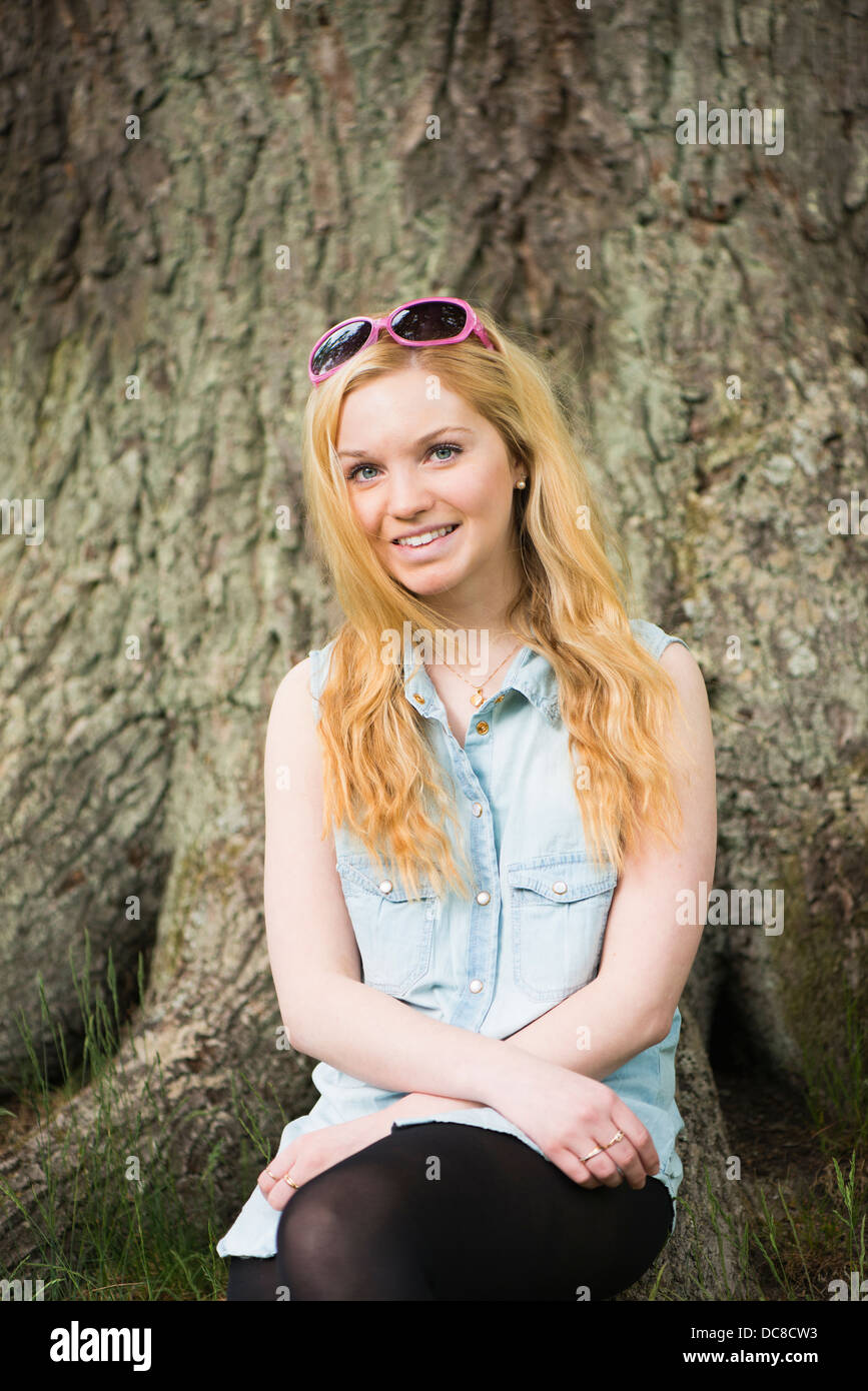 One young blonde attractive woman in front of big tree in a park Stock Photo