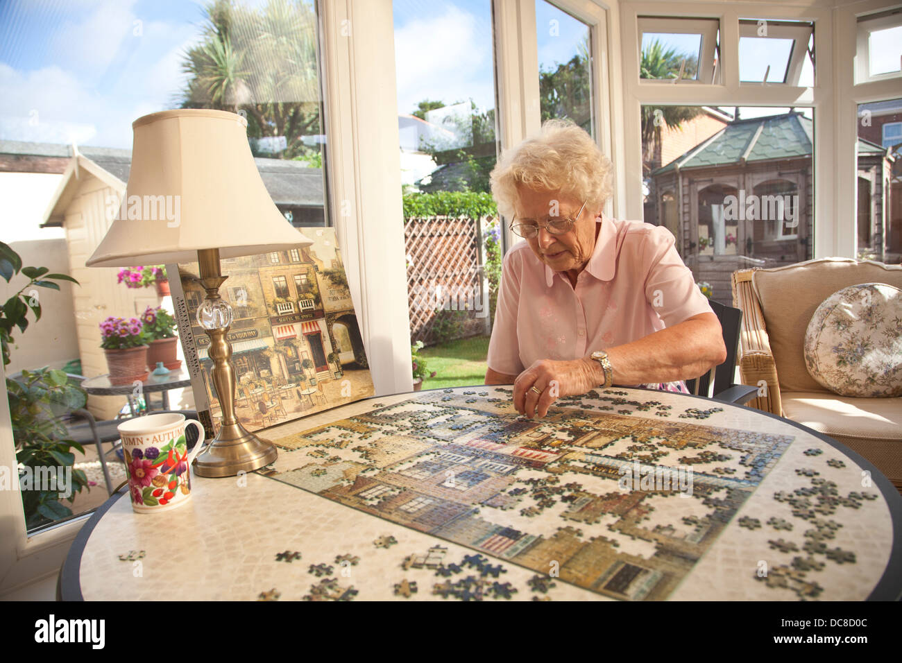 Retired woman making a jigsaw puzzle in her conservatory whilst enjoying a modest standard of living in England, United Kingdom Stock Photo