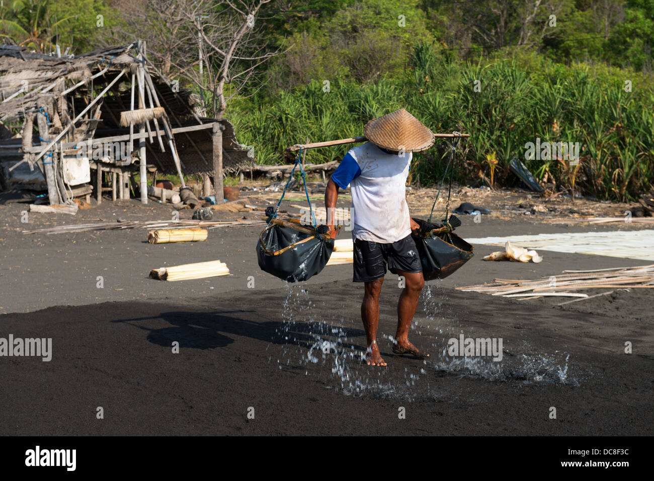 Manual male worker spreads sea water on black volcanic sand Stock Photo
